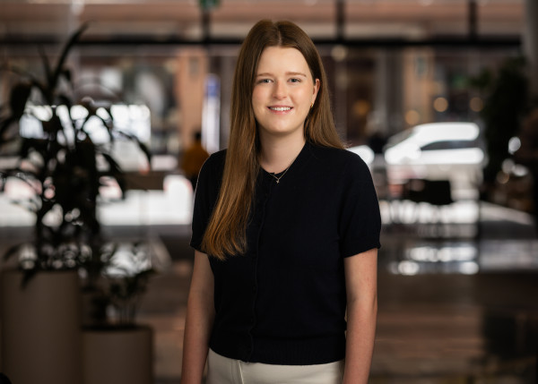 Bella smiling in her staff photo. Also there's a car and a tree.